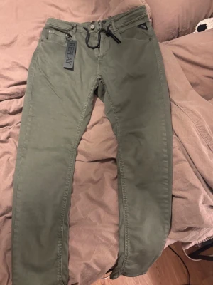 Olivgröna chinos från Replay XL - Snygga olivgröna chinos från Replay i storlek XL. Byxorna har en klassisk rak passform, två framfickor och två bakfickor. Tillverkade i ett mjukt och slitstarkt bomullsmaterial med knapp- och dragkedjegylf + snörning. Perfekta för en avslappnad men stilren look.