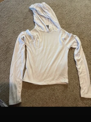 Vit hoodie med huva - Säljer en enkel och stilren vit hoodie med lång ärm och huva. Hoodien är tillverkad i ett mjukt och stretchigt material som känns skönt mot huden. Perfekt för dig som gillar en clean och avslappnad look.