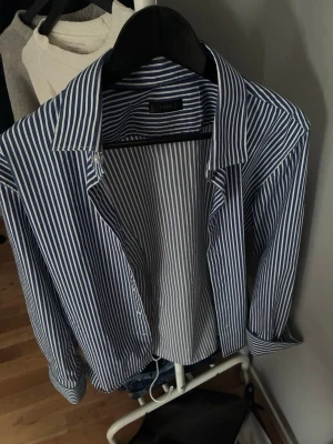 Blåvit randig skjorta - Säljer en klassisk blåvit randig skjorta med lång ärm och krage. Skjortan har knappar framtill och är tillverkad i mjuk bomull. 