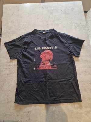 Svart Lil Boat 2 t-shirt Lil yachty  - Lil yachty merch                                                 Säljer en svart t-shirt med trycket 'LIL BOAT 2' och en röd profilbild på framsidan. T-shirten är i 100% bomull och har en klassisk passform med korta ärmar och rund hals. Perfekt för dig som gillar hiphop och streetwear.