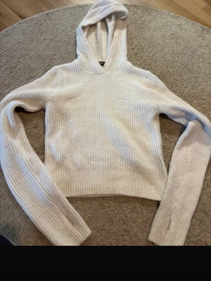 Vit stickad hoodie  - Säljer en vit ribbstickad hoodie från F8 med långa ärmar och huva. Tröjan har en croppad passform och tumhål i ärmsluten. Perfekt för dig som gillar en avslappnad och trendig stil. Materialet är mjukt och stretchigt för extra komfort.