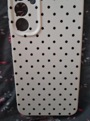 Vitt mobilskal med svarta prickar - SAMSUNG A25 SKAL.Snyggt vitt mobilskal med svarta prickar i ett klassiskt polka dot-mönster. Skalet är gjort i mjukt silikonmaterial och har utskärningar för kamera och knappar. Passar dig som vill ha ett stilrent men lekfullt skydd till mobilen.