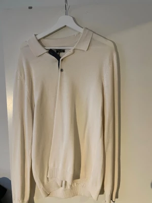 Beige pikétröja med lång ärm Massimo Dutti - Stilren beige pikétröja med lång ärm och klassisk krage. Tröjan har två knappar vid halsen och ribbade muddar vid ärmslut och nederkant. Perfekt för en clean och avslappnad look.