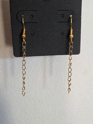 Guldiga kedjeörhängen i rostfritt stål  - Säljer ett par coola örhängen med guldiga kedjor i rostfritt stål. De har en enkel och stilren design med tunna länkar som hänger fritt. Perfekta för dig som gillar minimalistiska accessoarer och vill ha något som sticker ut lite extra. 