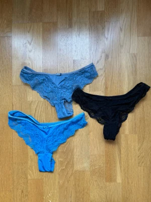 3-pack spets-trosor i blått och svart - Säljer ett 3-pack snygga trosor i spets, två i olika blå nyanser och en i svart. Alla har en feminin design med spetsdetaljer och liten rosett framtill. Perfekta för dig som gillar både färg och klassiskt svart. Materialet känns mjukt och stretchigt. Alla är oanvända då jag fick ett större pack men inte gillade passformen på dem, dem använda är exkluderade från dessa.