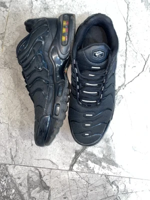 Nike Air Max Plus svarta sneakers - Nike Air Max Plus sneakers i helsvart med synlig Air Max-dämpning i sulan och vita detaljer på ovandelen. Skorna har en sportig siluett, skorna är använda och det är lite öppet där framme men inget man ser eller märker när man har på sig de 