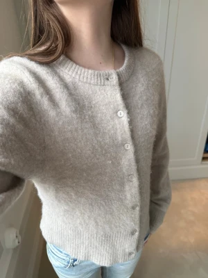 Beige kofta med slim fit - Mysig beige kofta från &other stories med rund halsringning och ribbade muddar. Koftan har en rak, något kortare passform och stängs med små vita knappar framtill. Tillverkad i ett mjukt, fluffigt material.