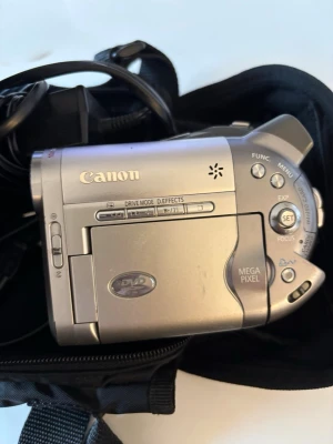 Canon DVD-videokamera silver - Säljer en silverfärgad Canon DVD-videokamera med megapixel-sensor och Dolby Digital Stereo Creator. Kameran har flera knappar för funktioner och menyer, samt plats för DVD-skivor. Kompakt design i metall och plast, perfekt för att spela in direkt på DVD.