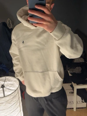 Vit hoodie - OBS storlek XL på lapp men passar L/M jag på bild har vanligtvis M!                                         Snygg vit hoodie med klassisk huva och känguruficka. Diskret broderad logga på bröstet. Tillverkad i mjukt bomullsmaterial som känns riktigt skönt mot huden. Perfekt för dig som gillar stilrena och tidlösa plagg.