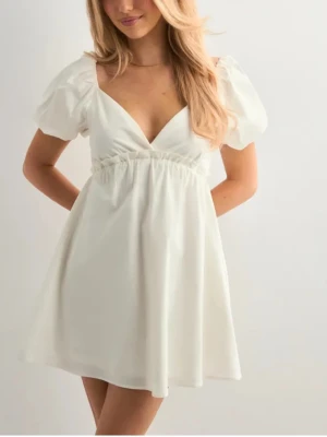 Student/skolavslutnings klänning - Superfin vit kort klänning med puffärmar och v-ringning. Funkar både som student eller skolavslutnings klänning. Klänningen är från Nelly och finns inte längre i denna storlek, pris lappen är kvar!