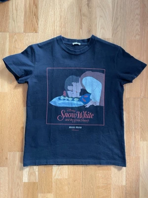  Miu Miu x Disney  T-shirt - Säljer en svart t-shirt från Miu Miu med Disney Snow White and the Seven Dwarfs-tryck framtill. Klassisk passform med korta ärmar och rund hals. Perfekt för dig som gillar coola prints och vill sticka ut lite extra.