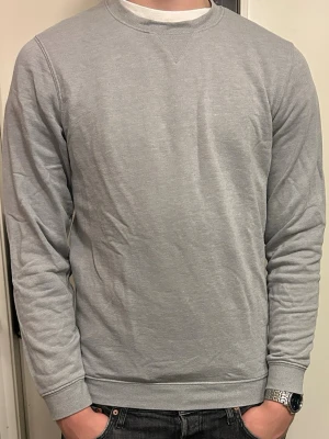 Ljusgrå tjocktröja - En stilren ljusgrå sweatshirt med rund halsringning och ribbade muddar vid ärmslut och nederkant. Tröjan har en enkel och clean design utan tryck eller logga, perfekt för en avslappnad look. Tillverkad i mjukt bomullsmaterial. 