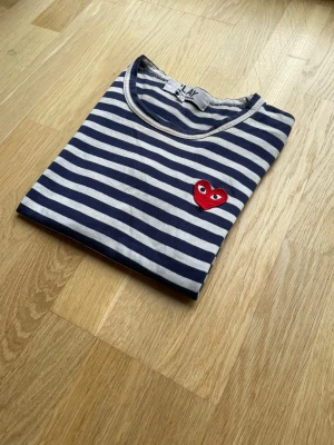 Comme des Garçons PLAY randig långärmad M - Perfekt klassisk randig långärmad från Comme des Garçons PLAY i storlek M. Ikoniska röda hjärtloggan fram. Äkta vara med originaltaggar (se bilder).  Skicket är mycket bra – inga fläckar, hål eller tvättslitage. Passar både herr och dam beroende på fit.  Nypris ligger runt 1500–2000 kr, så detta är ett riktigt bra kap.  📦 Snabb frakt 🚭 Rökfritt hem 💧 Nytvättad och fräsch