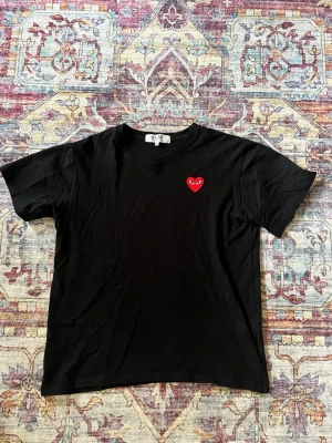 Svart t-shirt från Comme des Garçons - Svart t-shirt från Comme des Garçons. T-shirten har rund hals och korta ärmar, perfekt för en clean och stilren look. ÄKTA, storlek M och toppen till sommaren!