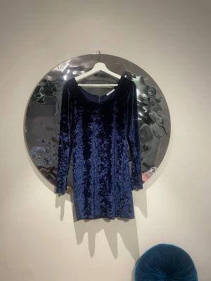 sammetsklänning - Snygg mörkblå sammetsklänning med lång ärm och rund halsringning. Klänningen har en kort passform och ett glansigt, mjukt material som ger en lyxig vibe. Perfekt för dig som vill ha något extra till din look.