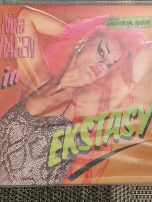 Nina Hagen – Ekstasy (Vinyl) - Säljer Nina Hagen – Ekstasy på vinyl. Skivan innehåller låtar som "Universal Radio", "Gods of Aquarius" och "Russian Reggae". Baksidan av omslaget visar en collage-design med olika bilder och text. Skivans framsida har ett porträtt av Nina Hagen med rosa hår. Inga repor. Utmärkt skick.