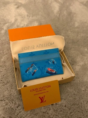 Snygg Blå kort hållare  - Säljer ett blått kortfodral med färgglada tryck av bilar och monogram. &nbsp;Tillverkad, troligen i läder, och levereras med original ask och dustbag. Perfekt sophi look för dig som vill ha något unikt i fickan.