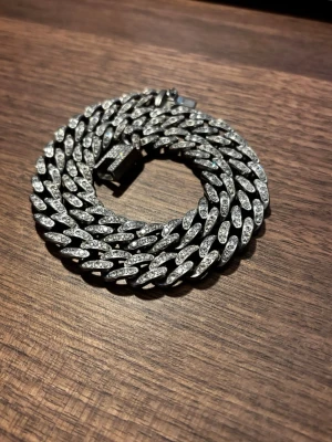 Silverfärgat halsband - Säljer ett chunky halsband, silverfärgat med massor av gnistrande stenar på varje länk. Låset är rektangulärt och också dekorerat med stenar. Perfekt för dig som vill sticka ut med ett riktigt statement-smycke.