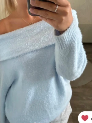 Ljusblå stickad off shoulder tröja - Supermjuk ljusblå stickad tröja med off shoulder-design. Tröjan har bred, nedvikt krage och långa ärmar. Tillverkad i fluffigt material som ger en cozy vibe och trendig look. Det står inte storlek men det passar M. Pris går att diskuteras