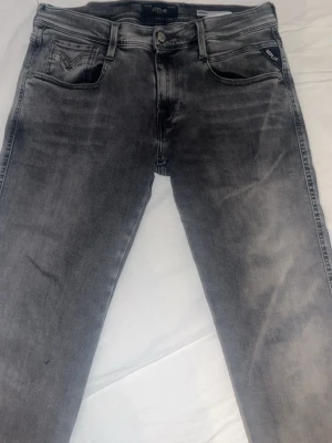 Grå slim fit jeans från Replay - Säljer ett par gråa slim fit jeans från Replay med snygg tvättad look. Jeansen har klassiska fem fickor, dragkedja och knapp i midjan samt Replay-logga på fickan. Perfekta för dig som gillar en modern och avslappnad stil. Knappt använda 