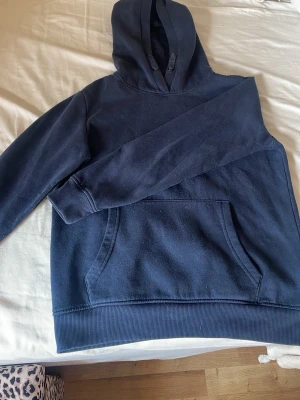 Mörkblå hoodie med magficka - En enkel och stilren mörkblå hoodie med huva och stor magficka framtill. Hoodien har ribbade muddar vid ärmslut och nederkant. Perfekt för en avslappnad look och passar till det mesta. Tillverkad i mjukt sweatshirtmaterial.