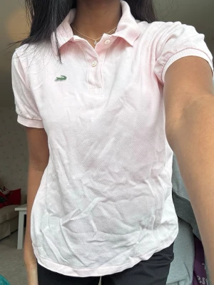Piké/t-shirt från Lacoste  - Ljusrosa/laxfärgad/aprikosfärgad piké från Lacoste. Fint skick i strl xs💕