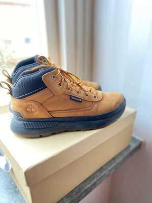 Bruna Timberland  - Säljer ett par snygga bruna Timberland  med svarta detaljer och robust svart sula. Skorna har klassiska gul- och orangefärgade snören, metallöljetter och vadderad krage i textil. Perfekta för dig som vill ha både stil och funktion. Nypris 1400 