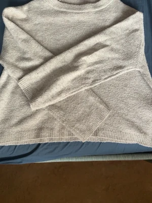 Ljusgrå stickad tröja med rund hals   - Mysig ljusgrå stickad tröja med rund halsringning och långa ärmar. Tröjan har en avslappnad passform och ribbstickade muddar vid ärmslut och nederkant. Perfekt för lager på lager under kyliga dagar.