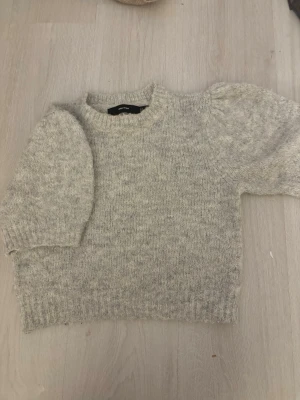 Ljusgrå stickad tröja med puffärm - Mysig ljusgrå stickad tröja med korta puffär growth och rund hals. Tröjan har en mjuk och fluffig känsla, ribbstickade muddar och en avslappnad passform. Perfekt för lager på lager och enkel att soppa till olika stilar.