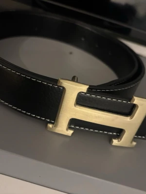 Svart bälte med ett guldigt H  - Svart, guldigt bälte alldrig använt 115 cm. Pris kan diskuteras .