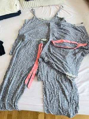 Grå prickig pyjamas med spetsdetaljer - Säljer ett set med grå pyjamas med vita prickar, består av linne, långa byxor och shorts. Både byxor och shorts har rosa dragsko i midjan och spetsdetaljer vid benslut. Materialet är mjukt och tunt, perfekt för att chilla hemma.