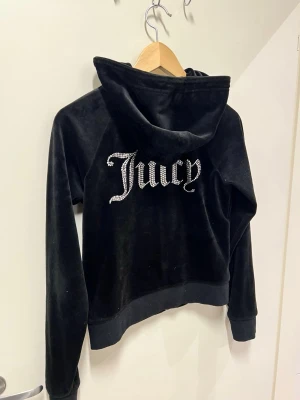 Juicy Couture Classic Velour hoodie  - Juicy Couture tröja säljes i fint skick  Storlek S. Svart velour färg.  Material klassisk mjuk velour. Diamantlogga på ryggen och en liten J logga framtill. Dragkedja med J-detalj.   Sömmen har gått upp lite på vänster ficka, behövs sy några stygn (se bild 5) - i övrigt mycket fint skick.   Nypris 1200kr