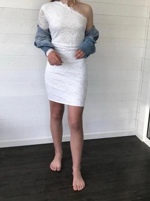 Vit spetsklänning med oneshoulder - Vit kort spetsklänning med oneshoulder och lång ärm på ena sidan. 