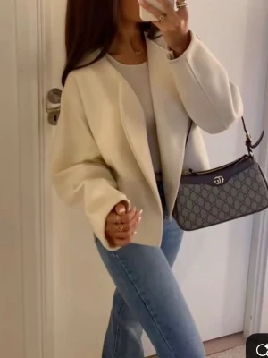 Krämvit cardiganjacka från ginatricot  - Stilren krämvit cardiganjacka från ginatricot med öppen front och raka, vida ärmar. Jackan har en minimalistisk design utan knappar eller dragkedja och är tillverkad i ett mjukt, strukturerat material. Perfekt att slänga över en topp för en clean look.