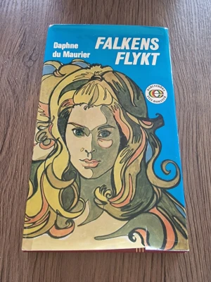 Falkens flykt av Daphne du Maurier - Falkens flykt är en skönlitterär roman av Daphne du Maurier med ett färgstarkt omslag i blått, gult och grönt. Boken har hårda pärmar och utspelar sig i en dramatisk universitetsmiljö med mystik och spänning.