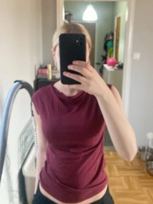 Mörkröd ärmlös topp i bomull - En enkel och snygg mörkröd topp med ärmlös design. Toppen har rund halsringning och är gjord i mjukt bomullsmaterial som känns skönt mot huden. Perfekt att matcha med jeans eller kjol för en avslappnad look.