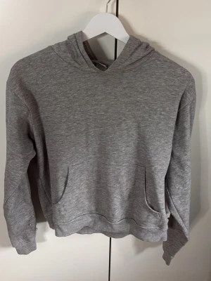 Grå hoodie med pärldetaljer - Snygg grå hoodie med huva och magficka. Ärmarna har coola pärldetaljer som ger en unik touch. Perfekt för en chill och avslappnad stil. Mjuk och skön bomullsblandning som passar året runt.