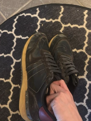 Svarta Valentino sneakers med nitar - Snygga svarta sneakers från Valentino med klassisk design och coola nitar på hälen. Skorna har svarta skosnören, svart ovandel i läder och textil samt beige sula. Perfekta för dig som gillar exklusiva och trendiga sneakers.