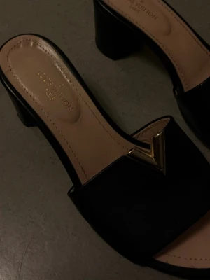 Svarta sandaler med klack - Snygga svarta sandaler från med öppen tå och bred rem. Dekorerade med en ikonisk guldfärgad V-detalj framtill. Sandalerna har en låg, stabil klack och beige innersula med. Perfekta för dig som gillar lyxig och stilren design. Använd 1-2 gånger. 