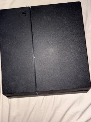 PlayStation 4 spelkonsol svart - PlayStation 4 spelkonsol från Sony i mattsvart plast med en stilren, rektangulär design och diskret PlayStation-logga på ovansidan. Perfekt för gaming och multimediaupplevelser.