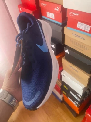 Blå Nike sneakers med ljusblå swoosh - Snygga blå sneakers från Nike med en ljusblå swoosh på sidan. Skorna har en sportig design med mesh-ovandel och vit sula som ger en fräsch look. Perfekta för dig som gillar stilrena och bekväma sneakers till vardags.