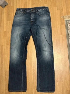 NUDIE Mörkblå raka jeans med slitningar - Säljer ett par sällsynta nudie jeans(easy Emil) med raka ben och snygga slitningar framtill. Passform är lite pösigare. Skick 9/10. Jeansen har klassisk femficksdesign och kontrastsömmar. Perfekta för en avslappnad och trendig look.  Materialet är denim i bomull.