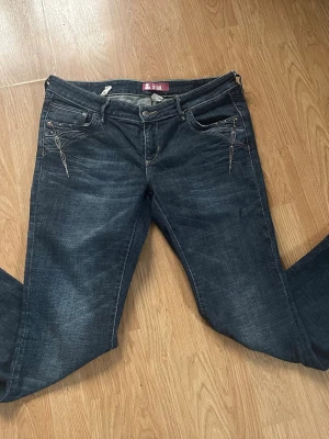 Mörkblå jeans från & Star - Snygga mörkblå jeans från & Star med flare ben och dekorativa sömmar på fickorna fram. Klassisk femficksmodell i denim med lätt slitningseffekt. Perfekta för dig som vill ha en stilren men ändå unik look.