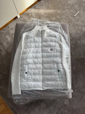 Vit Moncler dunjacka med ribbade ärmar - Vit Moncler Cardigan med quiltat mönster och ribbade ärmar. Jackan har två framfickor med knappstängning, dragkedja framtill och Moncler-logga på bröstet. Den är nyligen tvättad med kemtvätt och aldrig använd efter🧼👌🏼Det saknas däremot en dragkedja men inget som påverkar fitten.