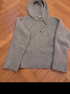 Grå hoodie från ZARA med huva - Mysig grå hoodie från ZARA i mjukt stickat material. Tröjan har huva med dragsko och breda ribbade muddar vid ärmslut och nederkant. Perfekt för en chill och avslappnad stil.