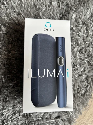 IQOS ILUMA i tobaksuppvärmare - Säljer en IQOS ILUMA i tobaksuppvärmare i stilren mörkblå färg. Setet innehåller både hållare och laddfodral, allt i en modern och smidig design. Perfekt för dig som vill ha ett alternativ till traditionella cigaretter.