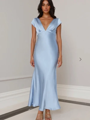Ljusblå balklänning satin - Elegant ljusblå långklänning i glansigt satinmaterial med djup v-ringning fram och öppen rygg med twistad detalj. Klänningen har korta ärmar och en figurnära passform som faller snyggt längs kroppen. Perfekt för speciella tillfällen. Nypris 900 kr❤️helt oanvänd med lappen kvar 