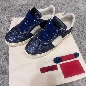 Valentino flycrews - Säljer mina mörkblåa glittriga flycrews. Fint skick men nästintill inga defekter. En nit saknas, men går att köpa. Storlek 38, innersula 25cm. Äkthetsbevis, extraskosnören och dustbag finns, ingen låda tyvärr. Köp direkt för 3250kr.  Lite små skador på lädret längst fram men inget som syns på håll 