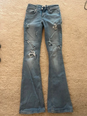 Skit snygga populära låg midjade blå jeans med hål - Säljer ett par blå lågmidjade bootcut jeans med hål. Jättebra skick andvända ett par fåtal gånger. Midjemåttet är 35 cm och innerbenslängden är 80 cm.
