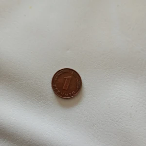 1 Pfennig mynt 1948 - Säljer ett tyskt 1 Pfennig kopparmynt från 1948, utgivet av Bank Deutscher Länder. Myntet har en ekkvist på ena sidan och valören 1 Pfennig på andra sidan. Perfekt för samlare av äldre mynt eller tysk valuta.